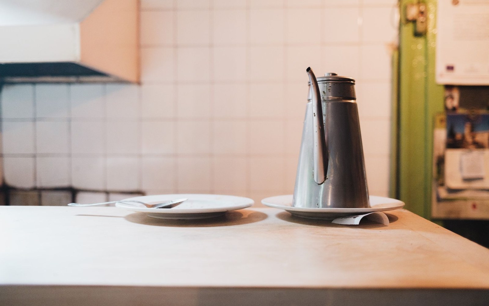 A metal coffee pot and empty plate sit on a café counter