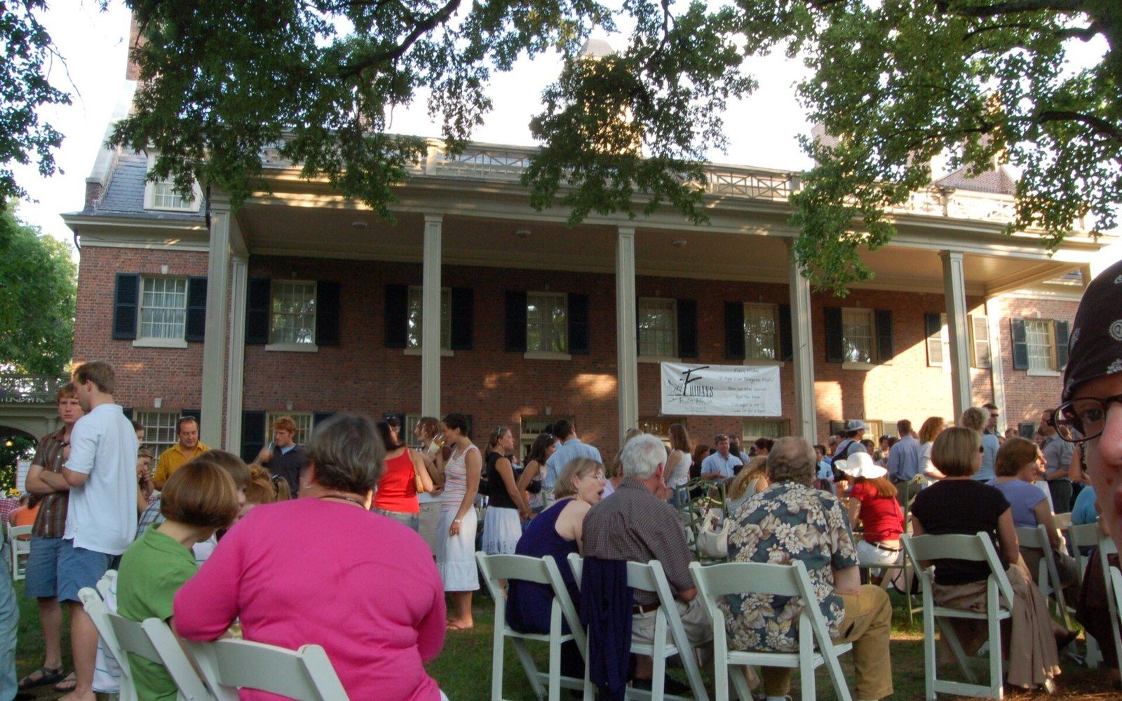 Crowd seated in folding chairs on a lawn outside a columned brick building