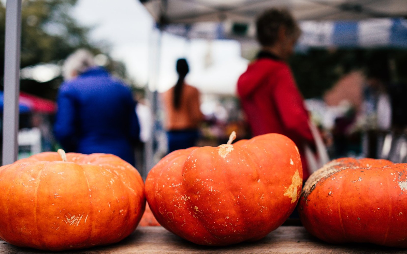 Orange pumpkins displayed on a table at an outdoor farmers market