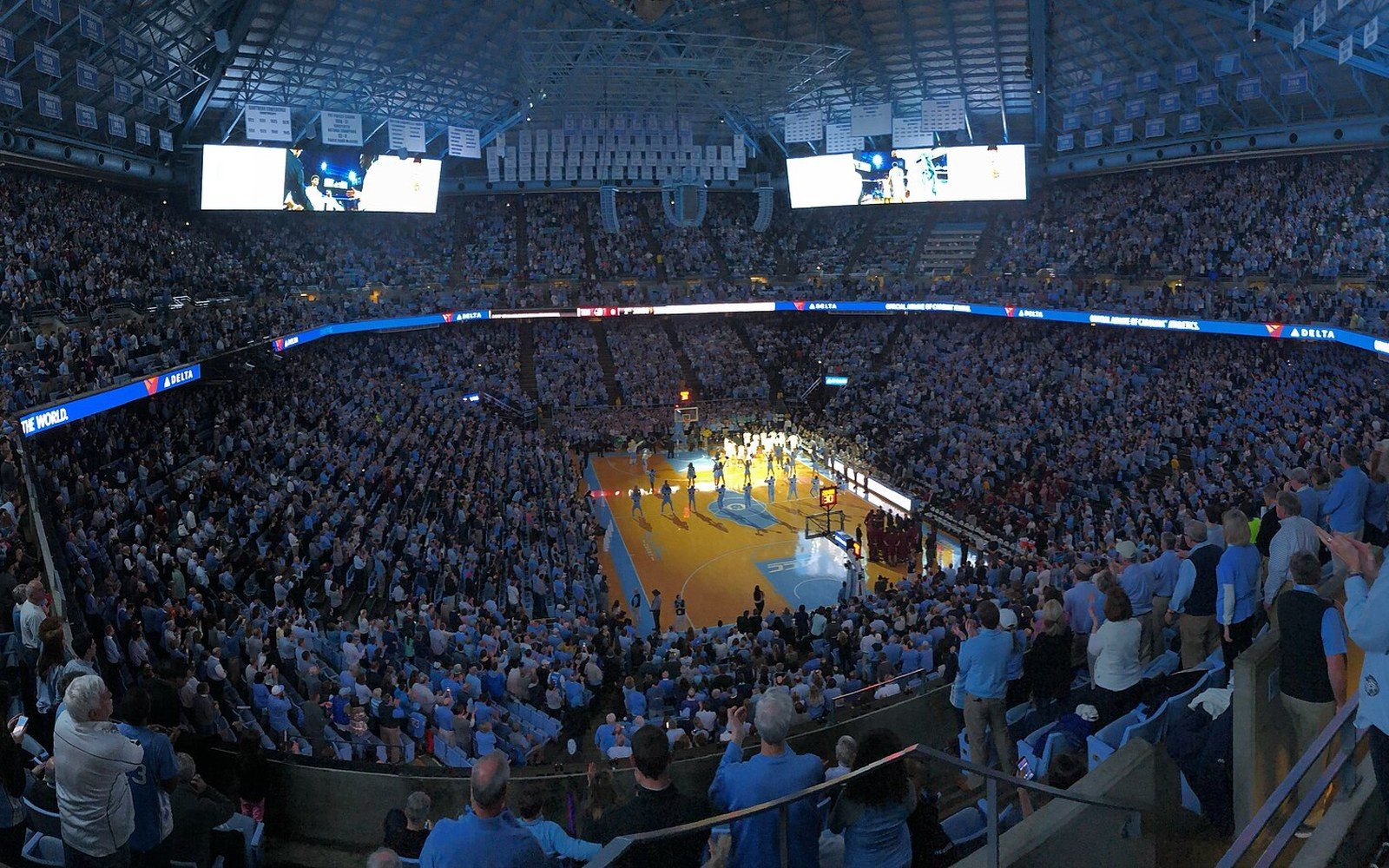 Packed arena crowd watches players on court during a college basketball game