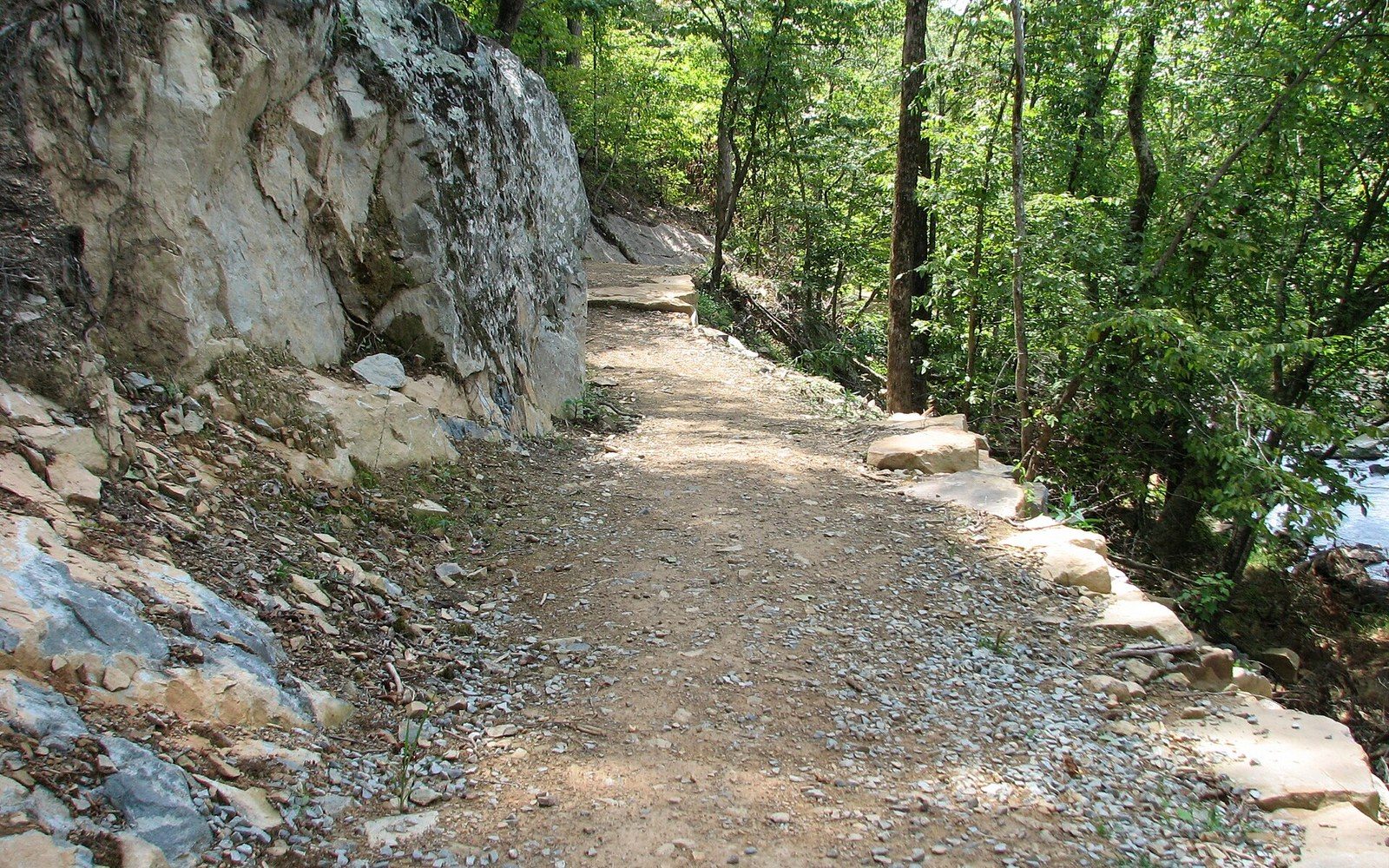 Gravel trail lined with stone edging runs beside a rock outcrop near Eno River