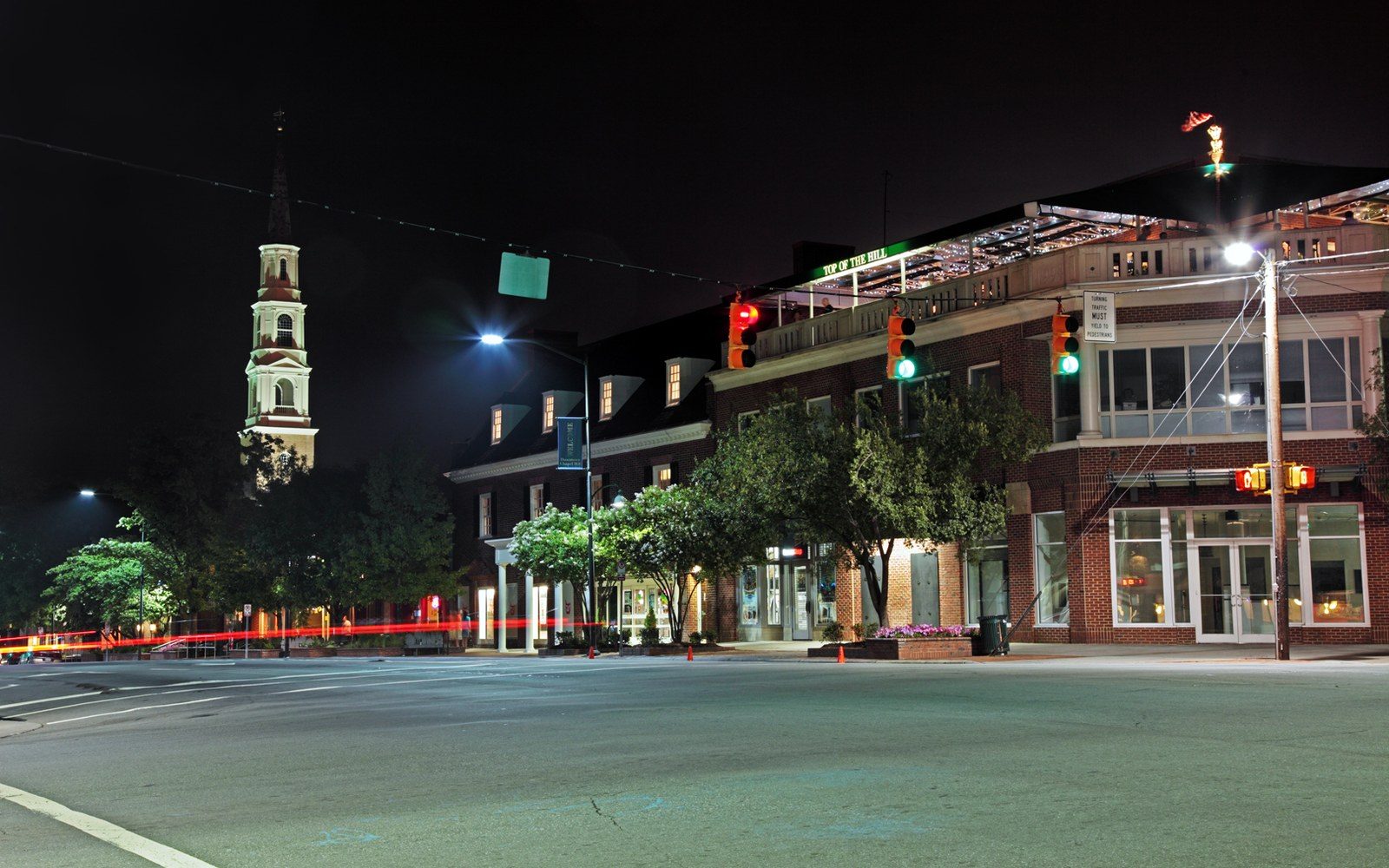 A quiet downtown street at night with an illuminated church steeple and brick storefronts