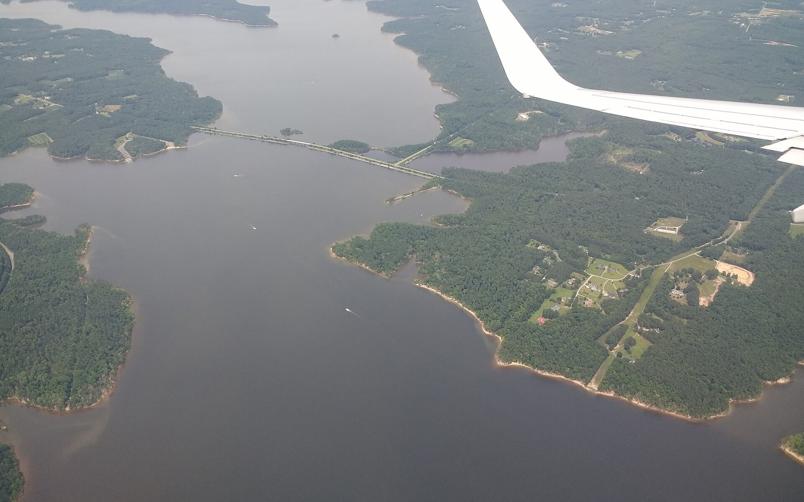Aerial view of a bridge crossing Jordan Lake with wooded shoreline and an airplane wing