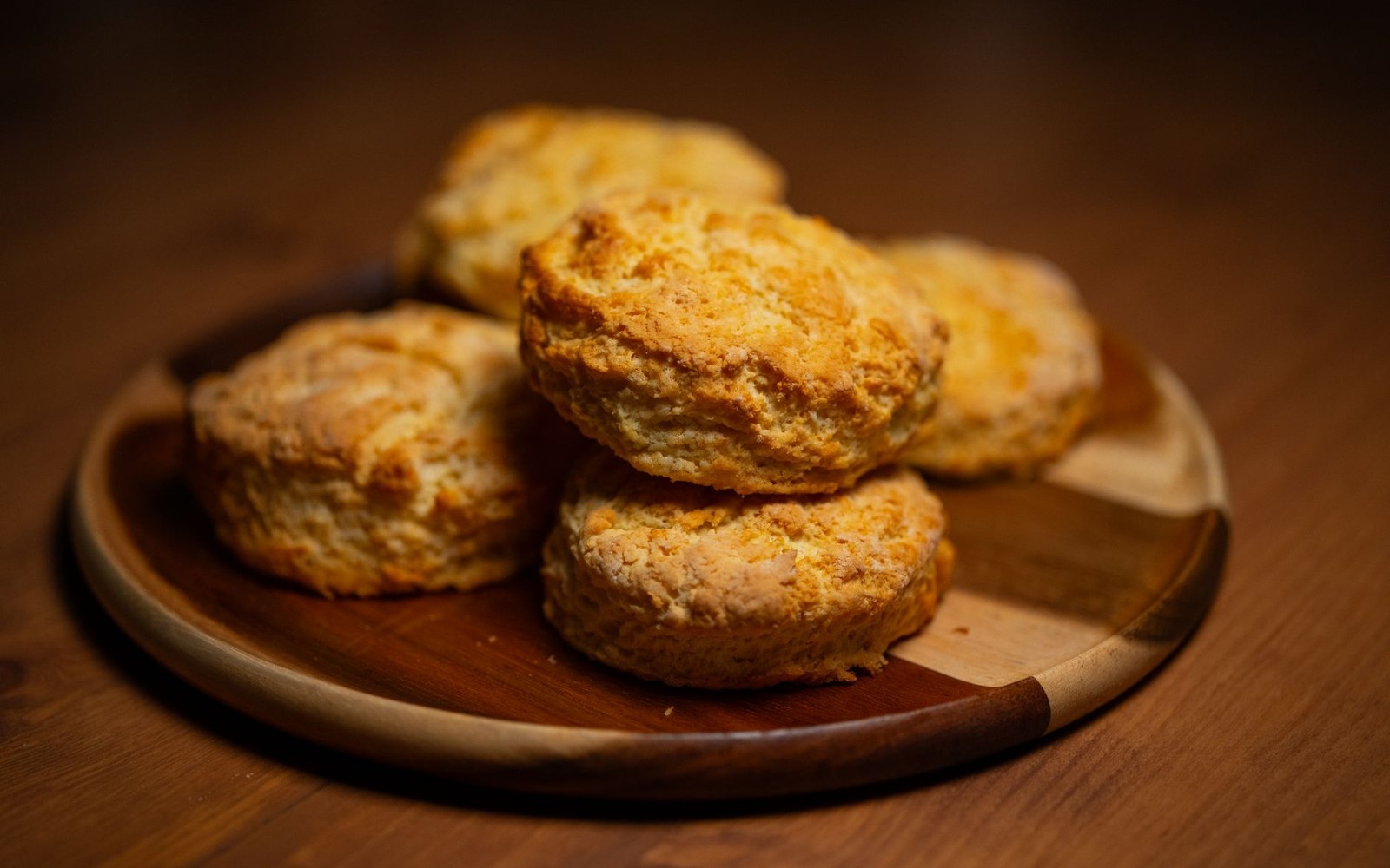 Five golden-brown biscuits stacked on a round wooden plate