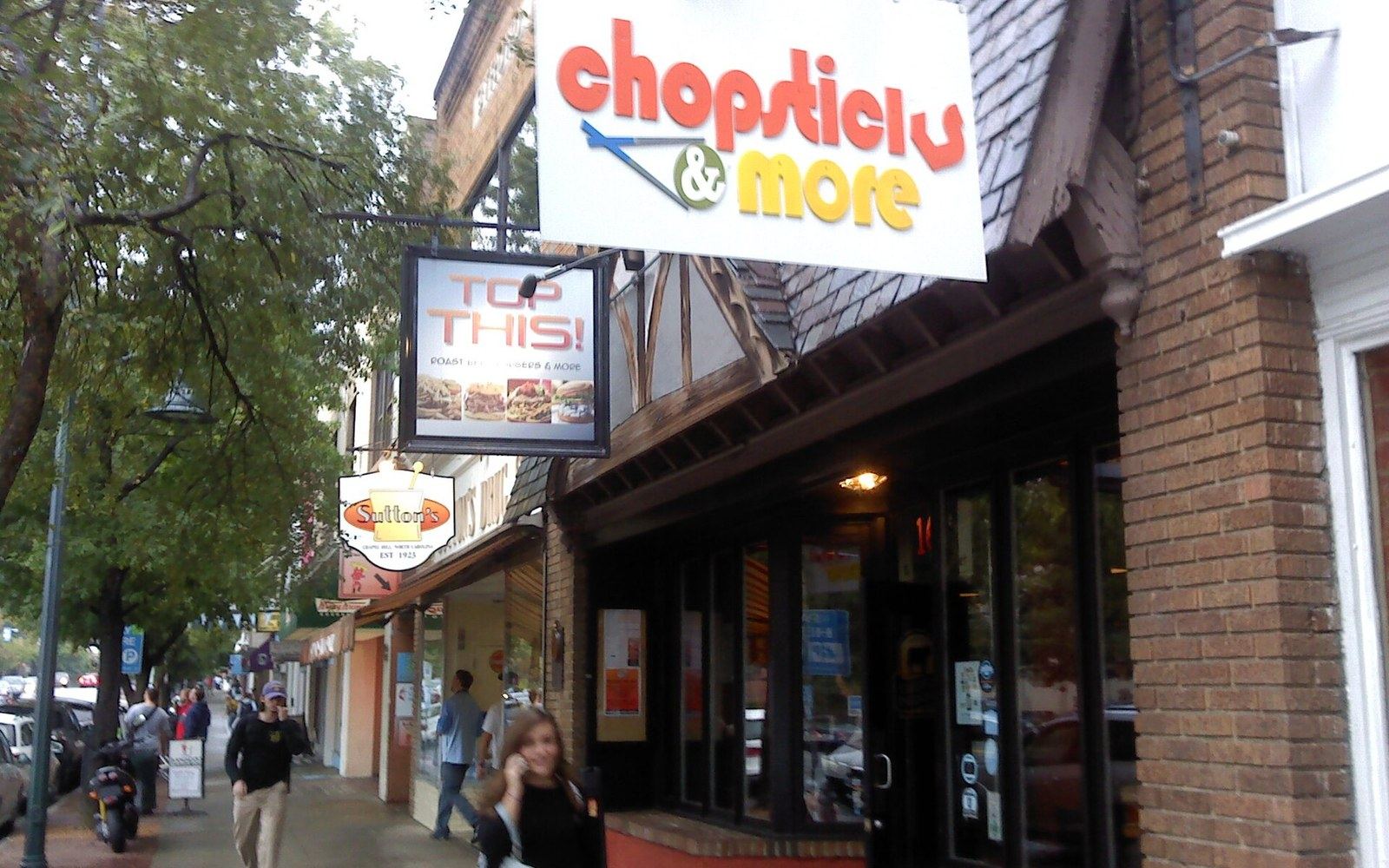 Storefront signs for Chopsticks & More and Top This restaurant along a tree-lined sidewalk