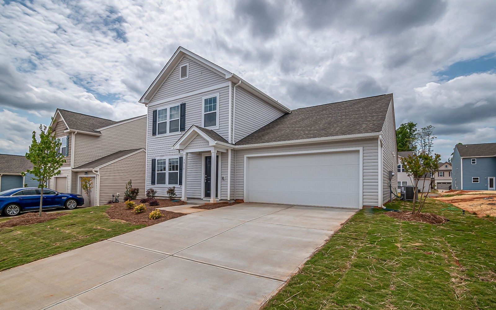 Two-story gray suburban house with attached garage and concrete driveway under cloudy sky