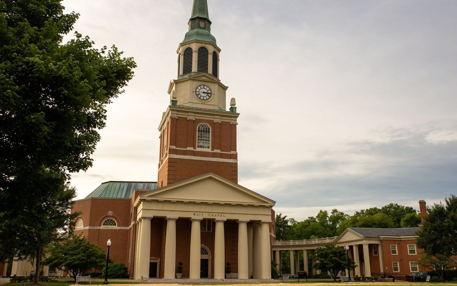 The Old Well under trees at McCorkle Place, early term, students crossing behind it