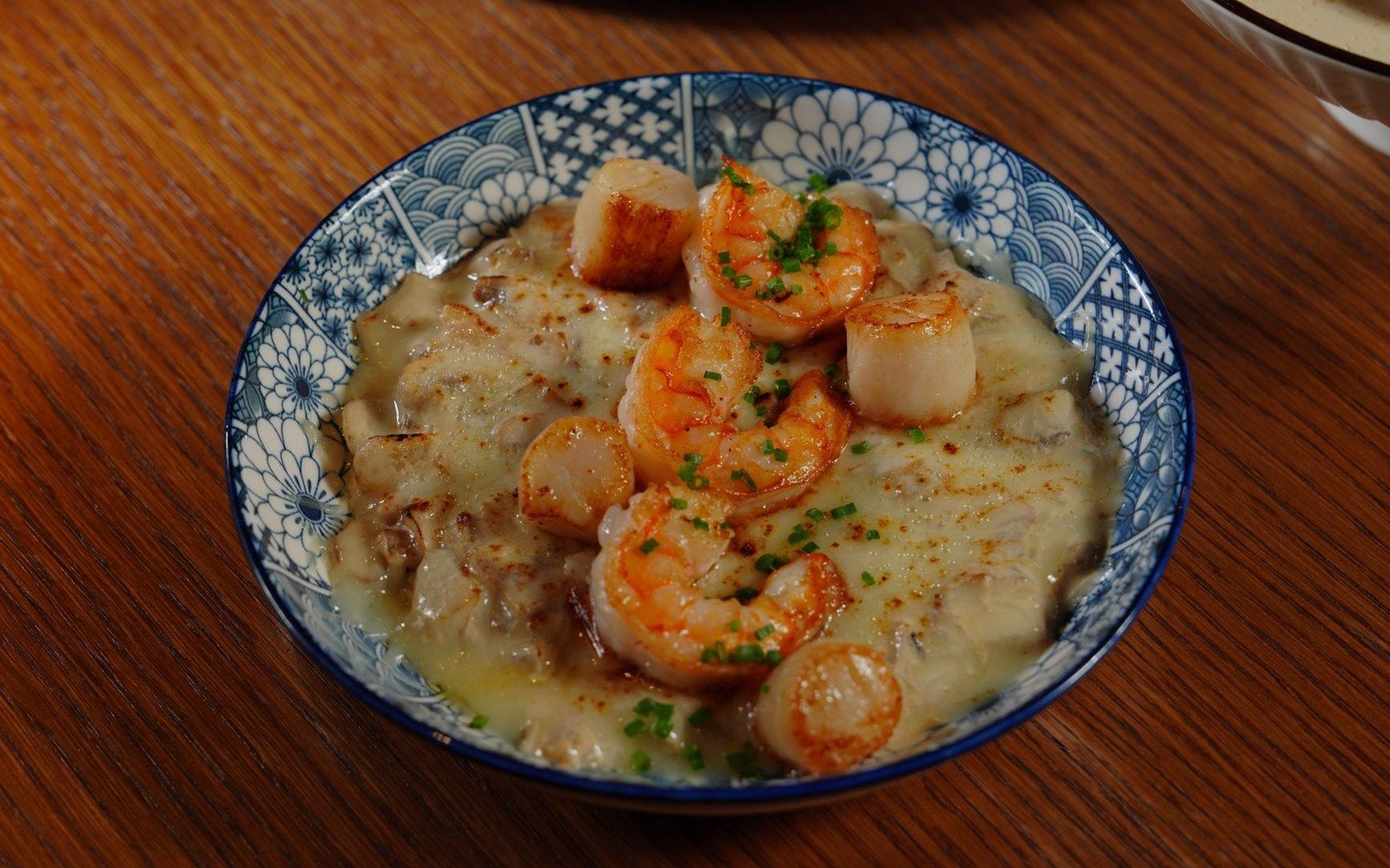 A bowl of shrimp and grits square on a worn wooden table, natural light, no props